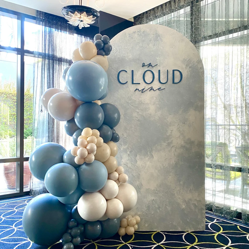 On Cloud Nine arched backdrop with dusty blue, sand, and cream balloon garland